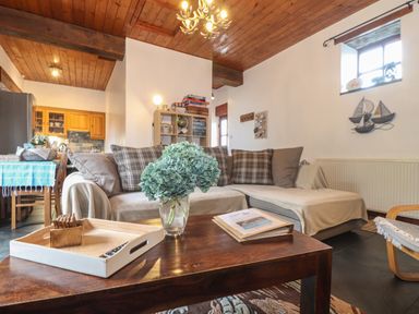 A living room with a sofa and coffee table next to a kitchen area at Owl Cottage in Ashen Cross Pelynt
