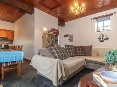 A living room with a sectional sofa and cushions next to a dining table with chairs at Owl Cottage in Ashen Cross Pelynt