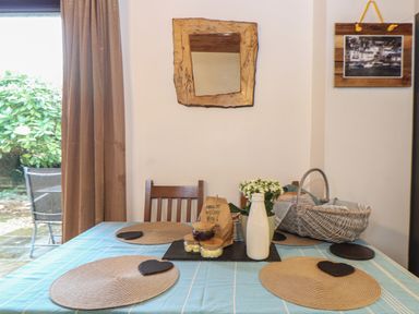 A dining table with placemats jars and a bottle next to a basket and a wooden chair at Owl Cottage in Ashen Cross Pelynt
