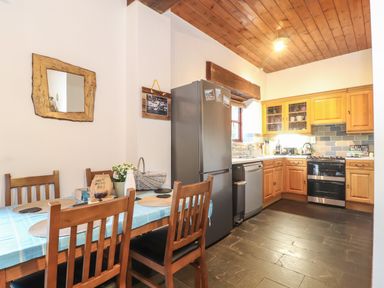 A kitchen with wooden cabinets a dining table with chairs and a refrigerator at Owl Cottage in Ashen Cross Pelynt