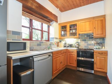 A kitchen with wooden cabinets stainless steel appliances and a window above the sink at Owl Cottage in Ashen Cross Pelynt