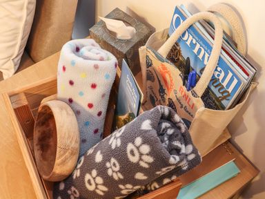 A wooden tray with rolled blankets a wooden bowl a tissue box and a bag with magazines on a wooden table at Owl Cottage in Ashen Cross Pelynt