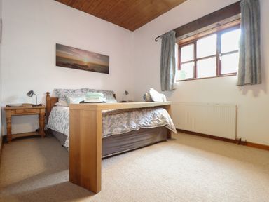 A bedroom with a double bed bedside tables lamps a window and a wooden bench at Owl Cottage in Ashen Cross Pelynt