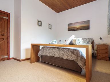 A bedroom with a wooden bed frame folded towels on the bed a wooden nightstand and a wooden door at Owl Cottage in Ashen Cross Pelynt