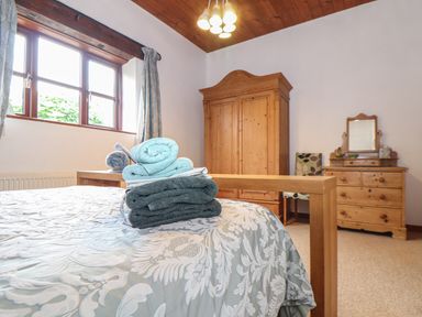 A bedroom with a bed folded towels a wooden wardrobe a dresser with a mirror and a chair at Owl Cottage in Ashen Cross Pelynt