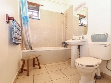 A bathroom with a bathtub shower combination a toilet a pedestal sink a small wooden stool and a towel hanging on a wall at Owl Cottage in Ashen Cross Pelynt