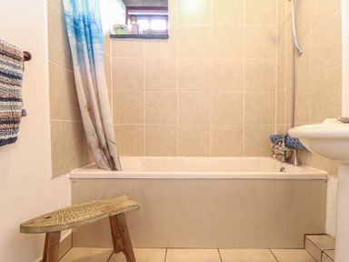 A bathroom with a bathtub shower curtain towel wooden stool and tiled walls at Owl Cottage Ashen Cross Pelynt