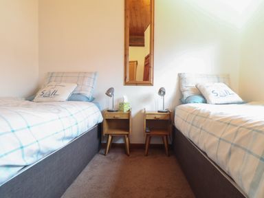 A bedroom with two single beds separated by two wooden nightstands with lamps and a mirror on the wall at Owl Cottage in Ashen Cross Pelynt
