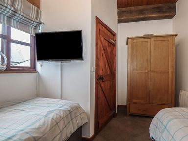 A bedroom with two single beds a wooden wardrobe a mounted TV and a wooden door at Owl Cottage in Ashen Cross Pelynt
