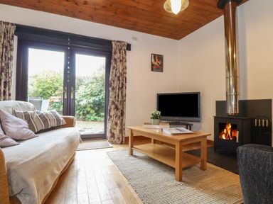 A living room with a sofa a wooden coffee table a television and a wood burning stove at Court Cottage Ashen Cross Pelynt