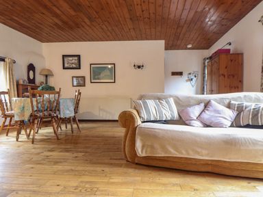 A living room with a wooden dining table and chairs a sofa with cushions wooden floor and ceiling at Court Cottage in Ashen Cross Pelynt