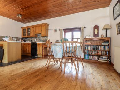 A kitchen and dining area with wooden floor and ceiling a dining table with chairs and a bookshelf at Court Cottage Ashen Cross Pelynt