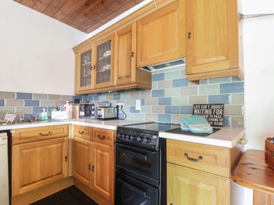 A kitchen with wooden cabinets a black oven a tiled backsplash and kitchen utensils at Court Cottage in Ashen Cross Pelynt