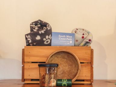 A wooden box with two rolled blankets and a South West Coast Path brochure with a wooden bowl a jar and a cylindrical container in front at Court Cottage Ashen Cross Pelynt