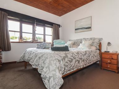 A bedroom with a bed beside a wooden nightstand and window at Court Cottage in Ashen Cross Pelynt