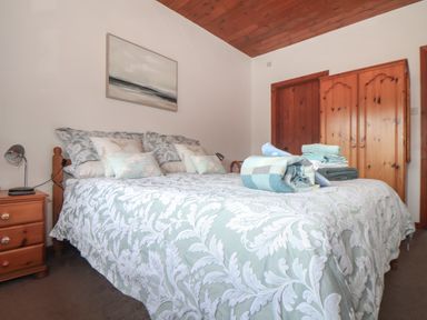 A bedroom with a bed covered in patterned bedding and folded towels a wooden wardrobe and a nightstand with a lamp at Court Cottage in Ashen Cross Pelynt