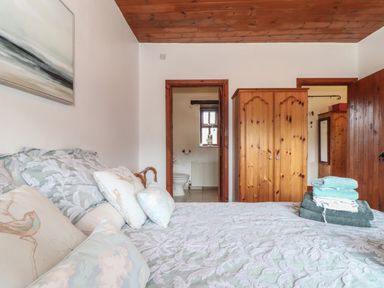 A bedroom with a bed pillows folded towels wooden wardrobe and an open door to a bathroom at Court Cottage in Ashen Cross Pelynt
