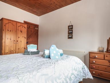 A bedroom with a wooden wardrobe wooden door wooden dresser and bed with folded towels and a blue hot water bottle at Court Cottage Ashen Cross Pelynt