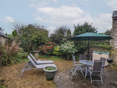 A garden with two lounge chairs a round table with chairs and an umbrella a barbecue and plants at Court Cottage Ashen Cross Pelynt