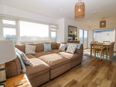 A living room with a brown sectional sofa and dining table in the background at Awel-Y-Mor in Trearddur Bay