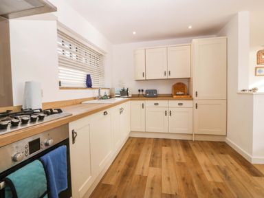 A kitchen with white cabinets wooden countertops and a gas stove with oven at Awel-Y-Mor in Trearddur Bay