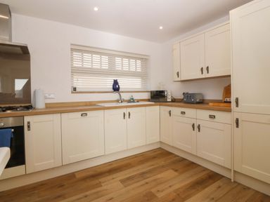 A kitchen with white cabinets wooden countertops a sink a microwave a toaster and wooden flooring at Awel-Y-Mor in Trearddur Bay