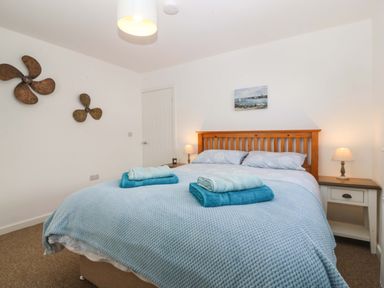 A bedroom with a wooden bed frame light blue bedding towels on bed two bedside tables with lamps and wall decorations at Awel-Y-Mor Trearddur Bay