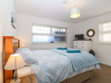 A bedroom with a double bed bedside lamps a chest of drawers and windows with blinds at Awel-Y-Mor in Trearddur Bay