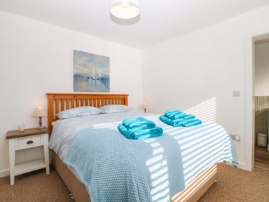 A bedroom with a double bed blue bedding and folded turquoise towels on the bed with two bedside tables and lamps and a painting above the bed at Awel-Y-Mor in Trearddur Bay