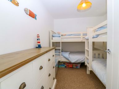 A small bedroom with bunk beds a white dresser and nautical decorations at Awel-Y-Mor Trearddur Bay