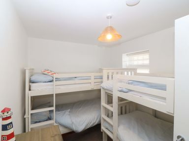 A small bedroom with two white wooden bunk beds and a wooden table with a lighthouse decoration at Awel-Y-Mor in Trearddur Bay