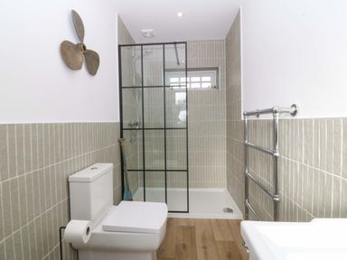 A bathroom with a shower, toilet, towel rack, propeller wall decoration, and wooden floor at Awel-Y-Mor in Trearddur Bay