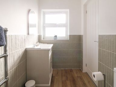 A bathroom with a sink cabinet a mirror a window wood flooring and a toilet paper holder at Awel-Y-Mor in Trearddur Bay