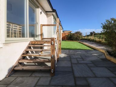 A wooden staircase leading to a patio with stone tiles and artificial grass at Awel-Y-Mor in Trearddur Bay