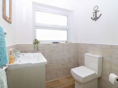 A bathroom with a white sink, white toilet, window, and an anchor decoration on the wall at Awel-Y-Mor in Trearddur Bay