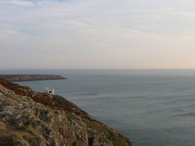 A rocky coastal cliff with a small white building overlooking the ocean at Awel-Y-Mor in Trearddur Bay