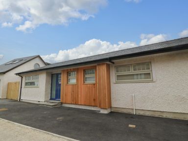 The exterior of a single-story house with a blue door and windows surrounded by wood paneling at Awel-Y-Mor in Trearddur Bay