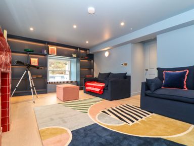 A living room with two blue couches a colorful rug a telescope and a built in shelving unit at Mavericks Wave in St Agnes