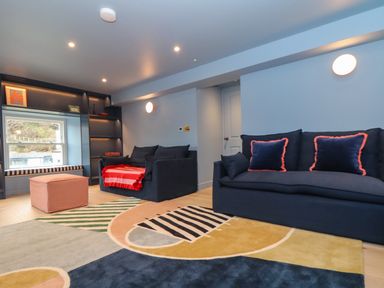 A living room with two navy sofas a colorful rug a pink ottoman and a window seat at Mavericks Wave in St Agnes