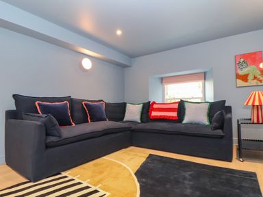 A corner sofa with cushions in a living room with a lamp and a window at Mavericks Wave in St Agnes