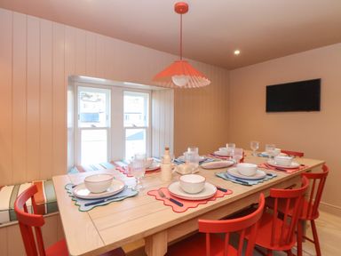 A dining room with a wooden table set with plates bowls glasses and cutlery with red chairs and a window seat at Mavericks Wave in St Agnes