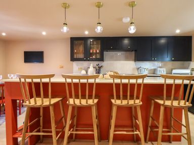 A kitchen with an orange island and wooden bar stools under hanging lights with black cabinets in the background at Mavericks Wave in St Agnes