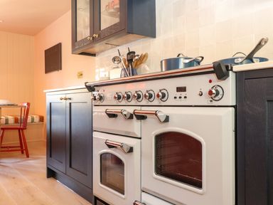 A kitchen with a white double oven stove black cabinets utensils on the countertop and a red chair with a cushioned bench at Mavericks Wave in St Agnes