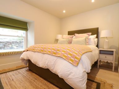 A bedroom with a bed a bedside table with lamp and a window with green blinds at Mavericks Wave in St Agnes