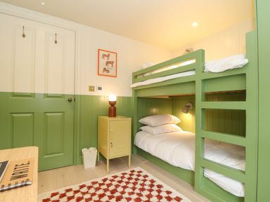 A bedroom with green bunk beds a lamp on a yellow cabinet and a patterned rug at Mavericks Wave in St Agnes