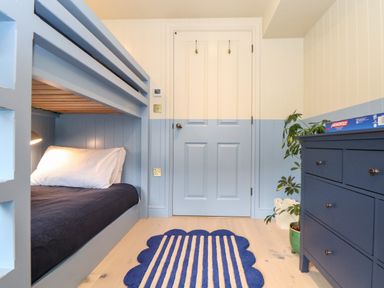 A bedroom with blue bunk beds a door a blue dresser a green plant and a blue rug at Mavericks Wave in St Agnes