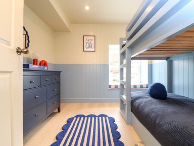 A bedroom with a bunk bed a blue dresser and a striped rug at Mavericks Wave in St Agnes