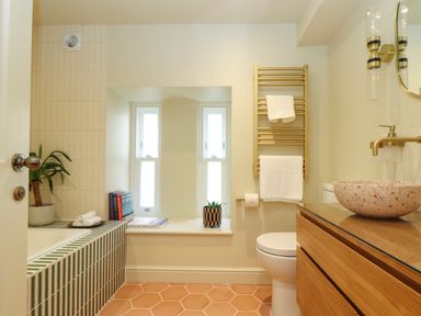 A bathroom with a bathtub tiled in green and white stripes a potted plant books on the windowsill a towel rack with white towels and a wooden vanity with a stone sink at Mavericks Wave in St Agnes