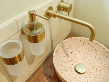 A bathroom sink with a terrazzo basin a wall-mounted brass faucet and matching soap dispenser and tumbler holder at Mavericks Wave in St Agnes