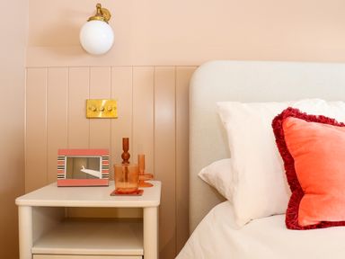 A bedside table with a photo frame, two orange glass holders, and a bed with white and orange pillows at Mavericks Wave in St Agnes